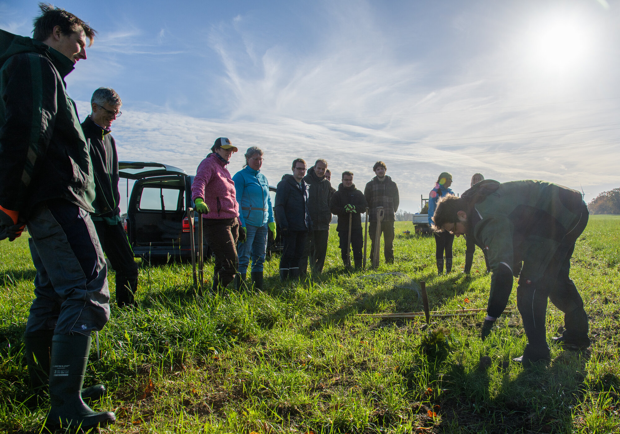 Felix Schmidt zeigt den Helfenden, wie die Gehölze gesetzt werden. Viele Personen stehen im Halbkreis um eine Person.